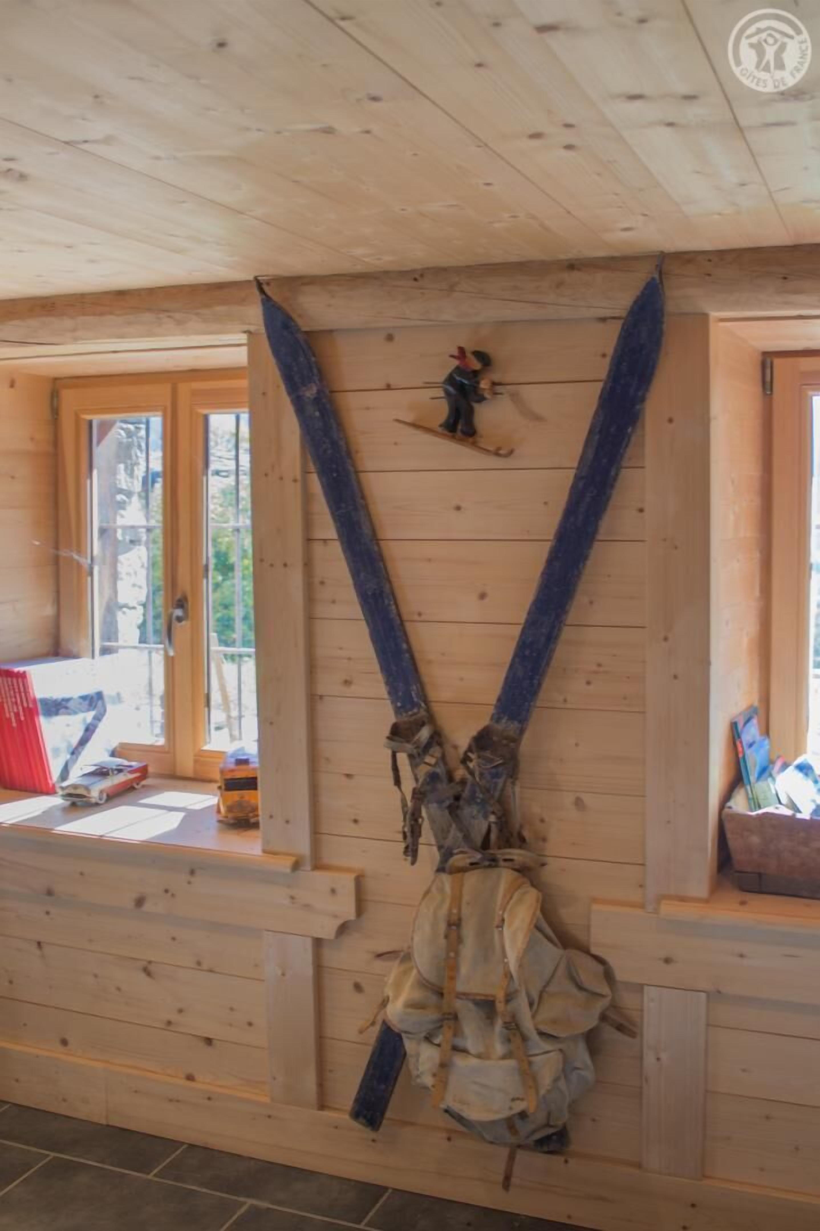Un intérieur en bois, avec une grande structure de poutres apparentes au plafond, une petite fenêtre et un banc en bois.