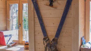Un intérieur en bois, avec une grande structure de poutres apparentes au plafond, une petite fenêtre et un banc en bois.