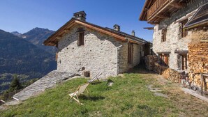 Un bâtiment en pierre doté d’un balcon en bois, entouré de montagnes.