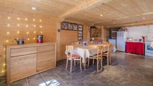 Un intérieur en bois comprenant une table à manger, des chaises, un coin cuisine et un mur décoré de guirlandes lumineuses.