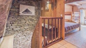 Une pièce rustique avec un mur en pierre, des poutres en bois, un lit superposé et un escalier doté d’une rampe en bois.