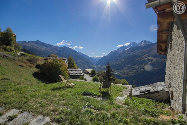 A mountainous landscape with a clear sky, a stone building, and a chair.