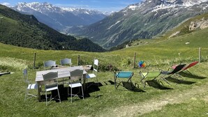 A dining area with a table and chairs set up on a grassy hillside with a mountain view. - LA CHIRA - VAL CENIS (VAL CENIS)