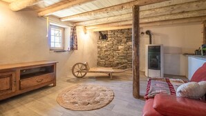 A rustic room with a stone wall, wooden beams, a vintage wooden cart, a red leather sofa, and a small table. - LA CHIRA - VAL CENIS (VAL CENIS)