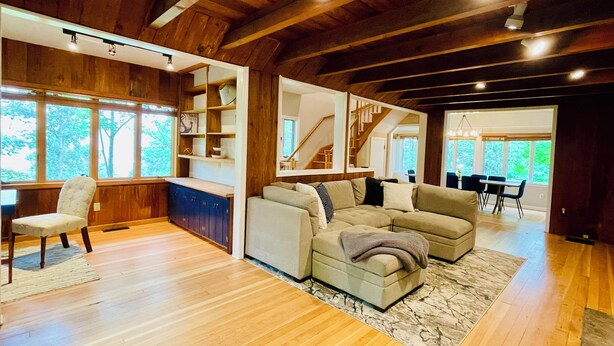 Ein geräumiges Wohnzimmer mit Holzböden, einer Sofagarnitur, einem Essbereich mit Tisch und Stühlen sowie einer Treppe zu einer weiteren Ebene.