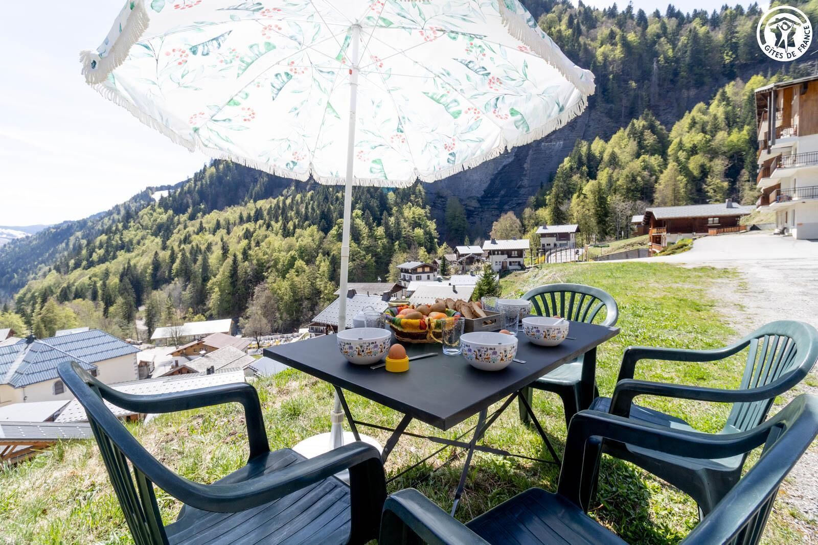 An outdoor dining area with a table, chairs, and a floral umbrella.