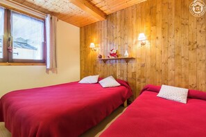 A room with two beds, wooden walls, a window with curtains, and a shelf with decorative items. - LES NIVEROLLES-LA BERGERONETTE (LA GIETTAZ)