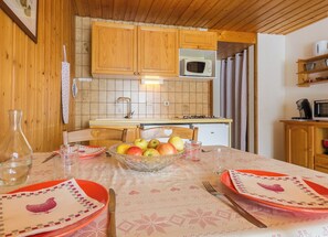 A cozy kitchen with wooden cabinets, a microwave, and a dining table set with plates and a fruit bowl. - LES NIVEROLLES-LA BERGERONETTE (LA GIETTAZ)