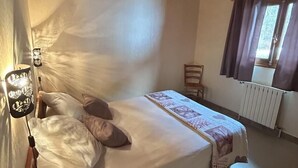 A bedroom with a wooden ceiling, a bed with pillows, a bedside table, a chair, and a window with curtains.