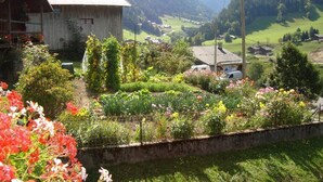 A rustic wooden house with a sloped roof, surrounded by a well-maintained garden with various flowers and plants.