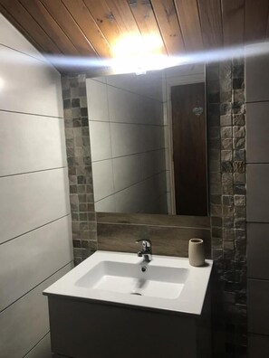 A bathroom with a white sink, a mirror, and a wooden ceiling.