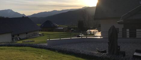 A rural setting with a house, a fenced area, and mountains in the background.