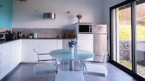 Una cuina moderna amb armaris blancs, una taula de dinar de vidre i vistes a l'exterior.