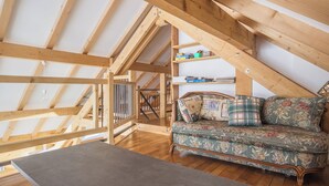 Ein Loft-Zimmer mit freiliegenden Holzbalken, Holzboden, einer Couch mit floralem Bezug und einem kleinen Tisch.