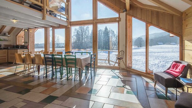 Ein geräumiges Zimmer mit großen Fenstern, einem Essbereich und Blick auf eine verschneite Landschaft.