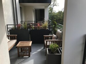 Relax on the balcony with a wooden table and comfortable seating, surrounded by lush greenery and a garden view.