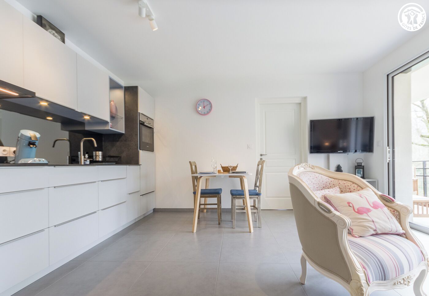 A modern kitchen with white cabinets, a coffee machine, and a dining area with a table and chairs.