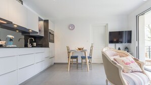 Moderni keittiö, jossa on valkoiset kaapit, kahvinkeitin sekä ruokailutila, jossa on pöytä ja tuolit.