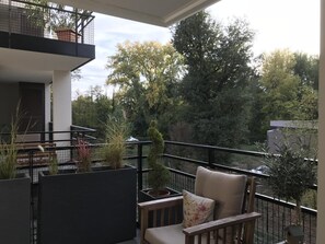 Relax on the balcony with a comfortable chair and table, surrounded by lush greenery and a serene view.