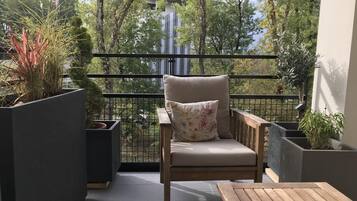 A balcony with a wooden chair and a small table, surrounded by potted plants and a metal railing.