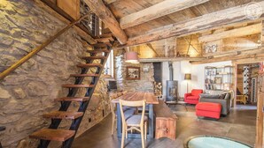 A rustic interior with a stone wall, wooden staircase, a dining area, a fireplace, and a red sofa.