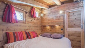 A cozy wooden room with a bed, striped pillows, and a window with curtains.