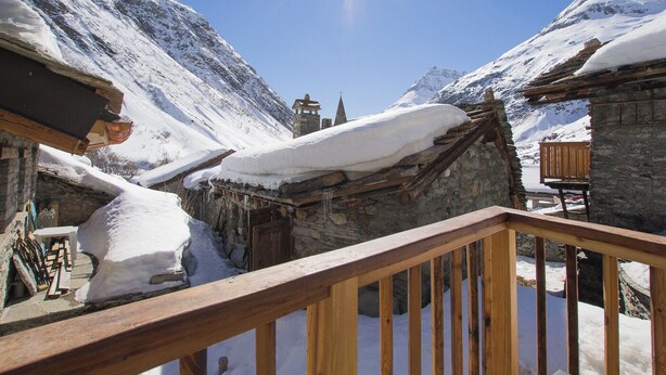 A snow-covered mountain village with stone buildings and wooden balconies.