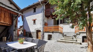 Ein Innenhof mit Tisch und Stühlen, Steinmauern, hölzernen Balkonen und einem Baum.