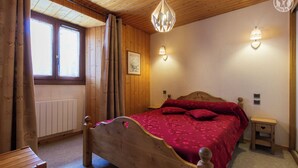 Ein Schlafzimmer mit Holzwänden, einem hölzernen Bett, einem Nachttisch und einem Fenster mit Vorhängen.
