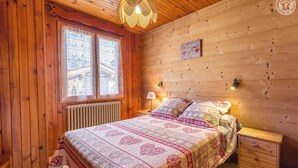 Une chambre à coucher aux murs lambrissés, avec un lit, des tables de chevet, une lampe et une fenêtre donnant sur un beau paysage.