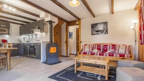 A modern kitchen with a wood-burning stove, a dining area with a table and chairs, and a cozy seating area with a sofa and ottoman. - LA CHARMETTE - LA ROSIERE MONTVALEZAN (LA ROSIERE MONTVALEZAN)