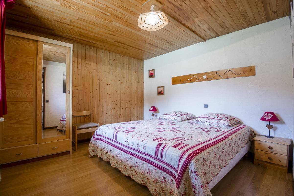 Une chambre avec un plafond en bois, un grand lit avec une literie à motifs floraux, une armoire en bois, un miroir et une œuvre d’art accrochée au mur.