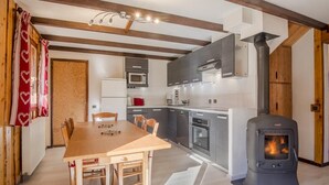 A modern kitchen with a wood-burning stove, a dining table, and a kitchen island. - LA CHARMETTE - LA ROSIERE MONTVALEZAN (LA ROSIERE MONTVALEZAN)