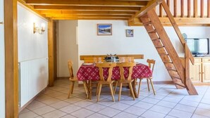 Uma escada de madeira leva a um andar superior, com uma sala de jantar, mesa e cadeiras, e uma cozinha com armários e uma televisão.
