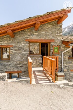 A stone building with a wooden staircase leading to a door, a bench outside, and a sign indicating it's a gite. - Le Canton - VAL CENIS (VAL CENIS)