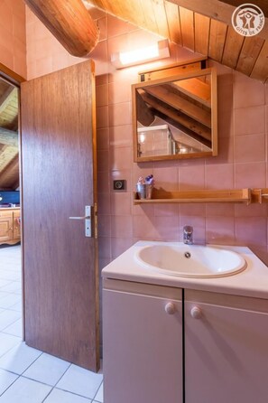 A bathroom with a wooden door, a sink, a mirror, and a shelf.