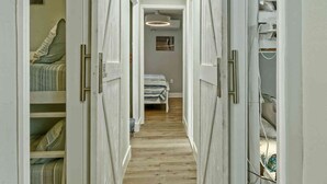Een smalle gang met witte kasten aan beide kanten, die leidt naar een slaapkamer met een bed en een plafondlamp.