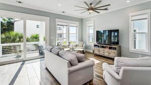 A spacious living room with a large sofa, a television, and a ceiling fan. - Calla Lily Cove : Breathtaking Home w/Elevator In a Gated Community-Sleeps 12 (Navarre)