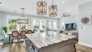 A spacious kitchen with a large island, pendant lighting, and a dining area with chairs and a table. - Calla Lily Cove : Breathtaking Home w/Elevator In a Gated Community-Sleeps 12 (Navarre)