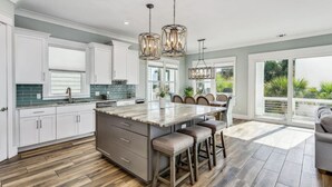 A modern kitchen with a large island, white cabinetry, and a dining area with a view. - Calla Lily Cove : Breathtaking Home w/Elevator In a Gated Community-Sleeps 12 (Navarre)