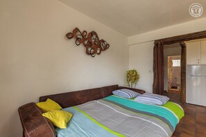 A bedroom with a bed, a wooden headboard, a wall-mounted abstract art piece, and a plant.