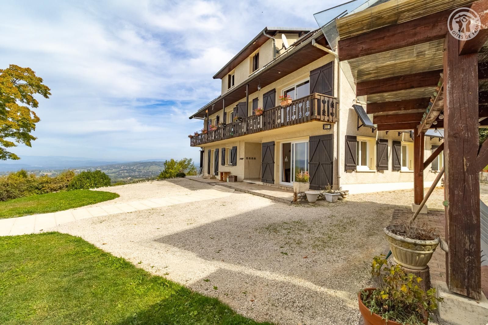 A multi-story building with a balcony, a gravel driveway, and a view of the countryside.