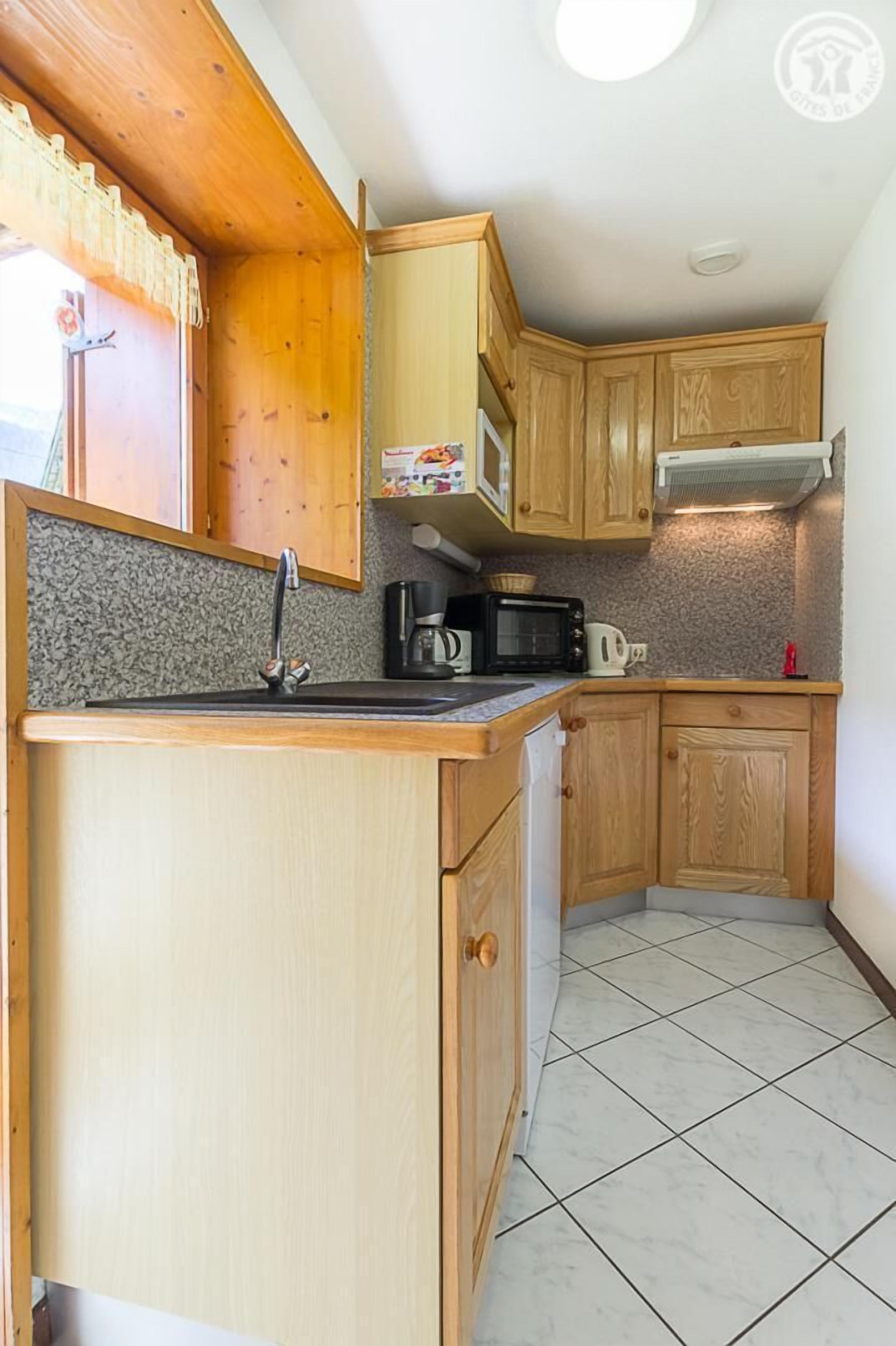 Cocina compacta con armarios de madera, microondas, hervidor y pileta.