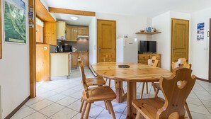 Un coin repas avec une table et des chaises en bois, une cuisine à l’arrière-plan et une affiche accrochée au mur.