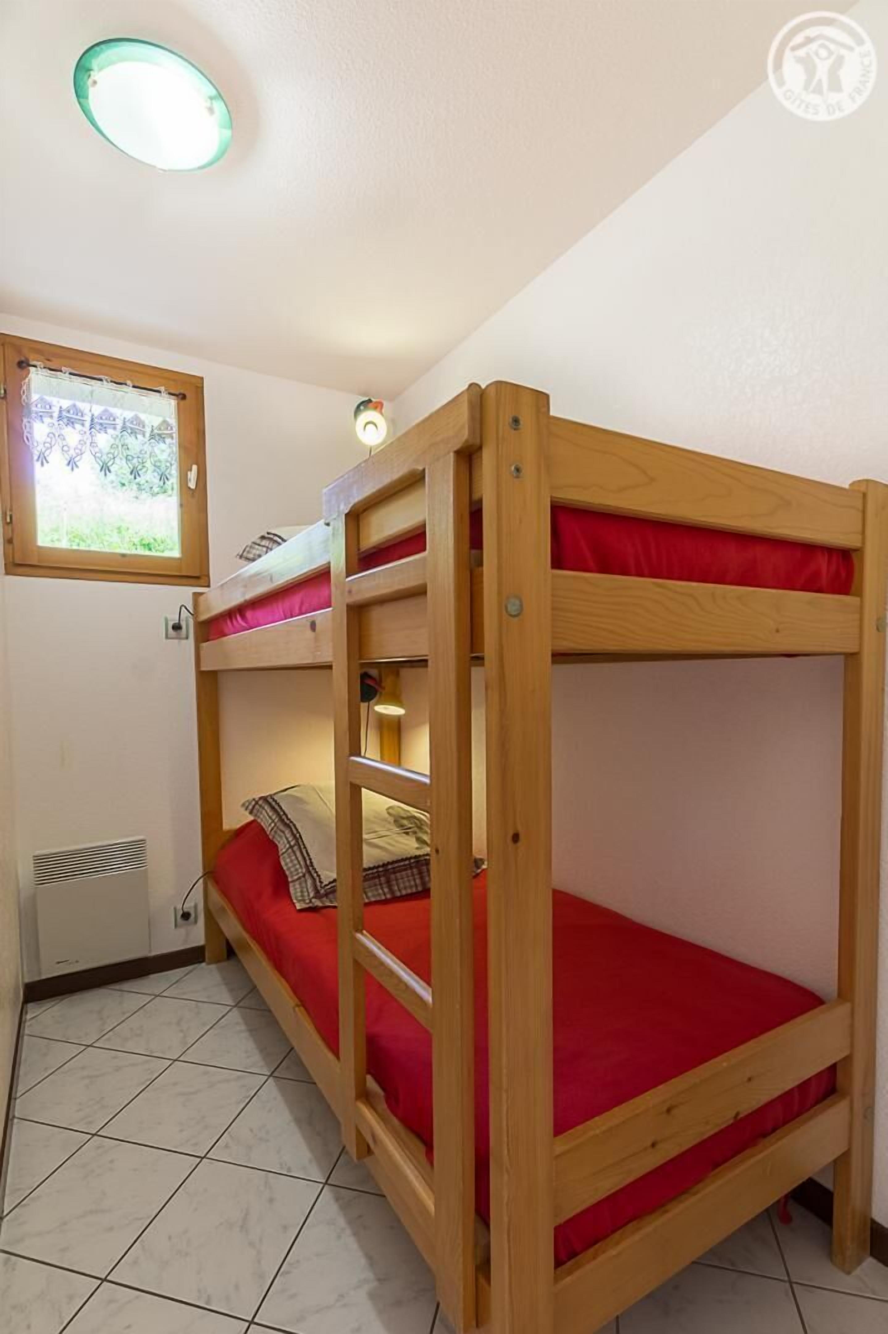 Dormitorio con literas, ventana y cubrecama rojo.