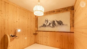 A wooden room with a bed, a wall-mounted lamp, and a painting of mountains. - LA METAIRIE DE MON PERE (LE PLANAY)
