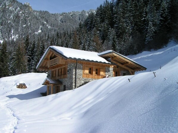 A wooden cabin with a stone foundation, set on a snow-covered slope with a forest backdrop. - LA METAIRIE DE MON PERE (LE PLANAY)