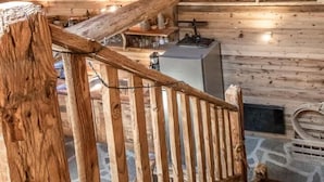 Eine HolztTreppe mit Geländer, die zu einem Raum mit Kamin und Steinwand führt.