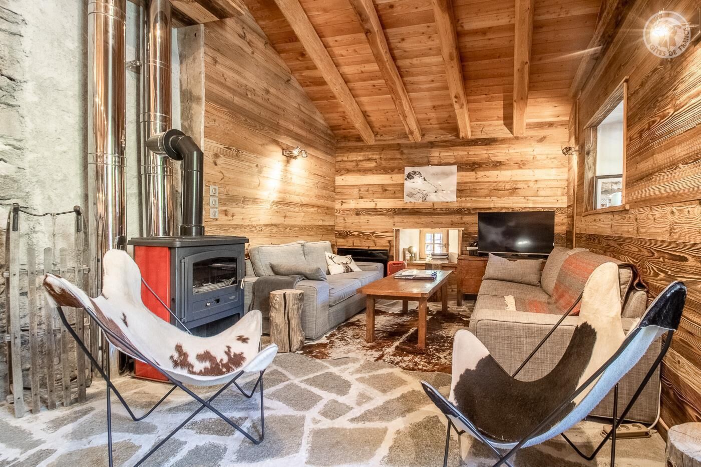 A cozy log cabin interior with a stone floor, a fireplace, a sofa, and a television.