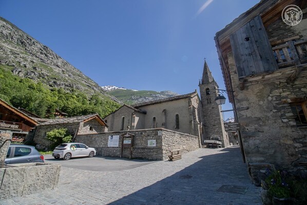 A stone building with a bell tower, a sign for a cooperative, and a car parked in front.